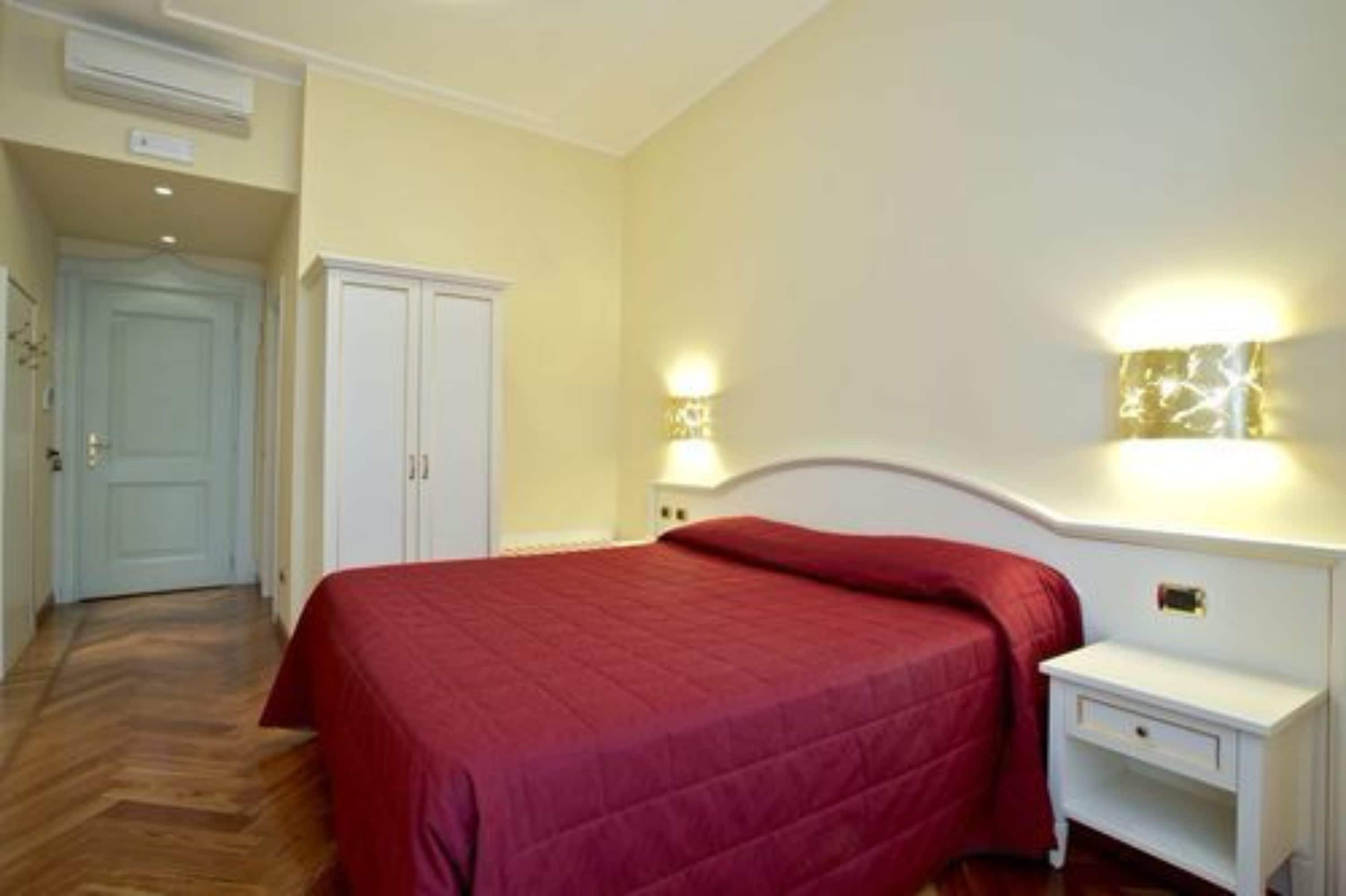 A bedroom with a bed, a nightstand, a wall-mounted lamp, and a wardrobe.