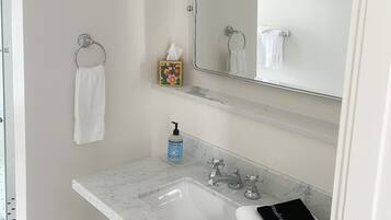 Un baño con lavamanos de mármol, un espejo, un perchero para toallas y un estante pequeño con una caja de pañuelos.