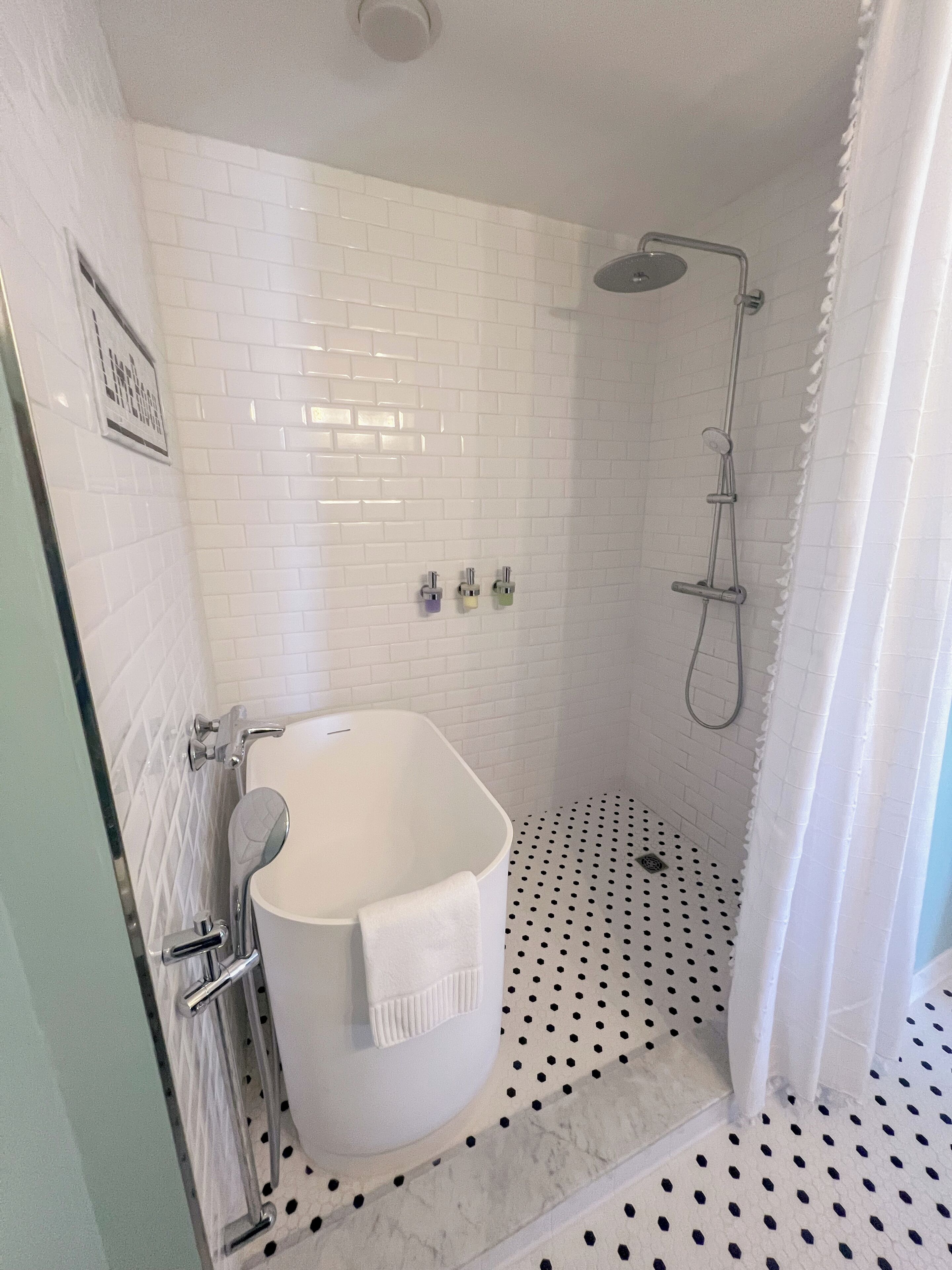 A bathroom with a freestanding bathtub, a shower with a handheld showerhead, and a tiled floor with a polka dot pattern.