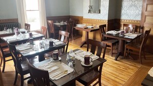 A dining area with wooden tables and chairs, set with white napkins, cutlery, and glassware. - LimeRock Inn (Rockland)