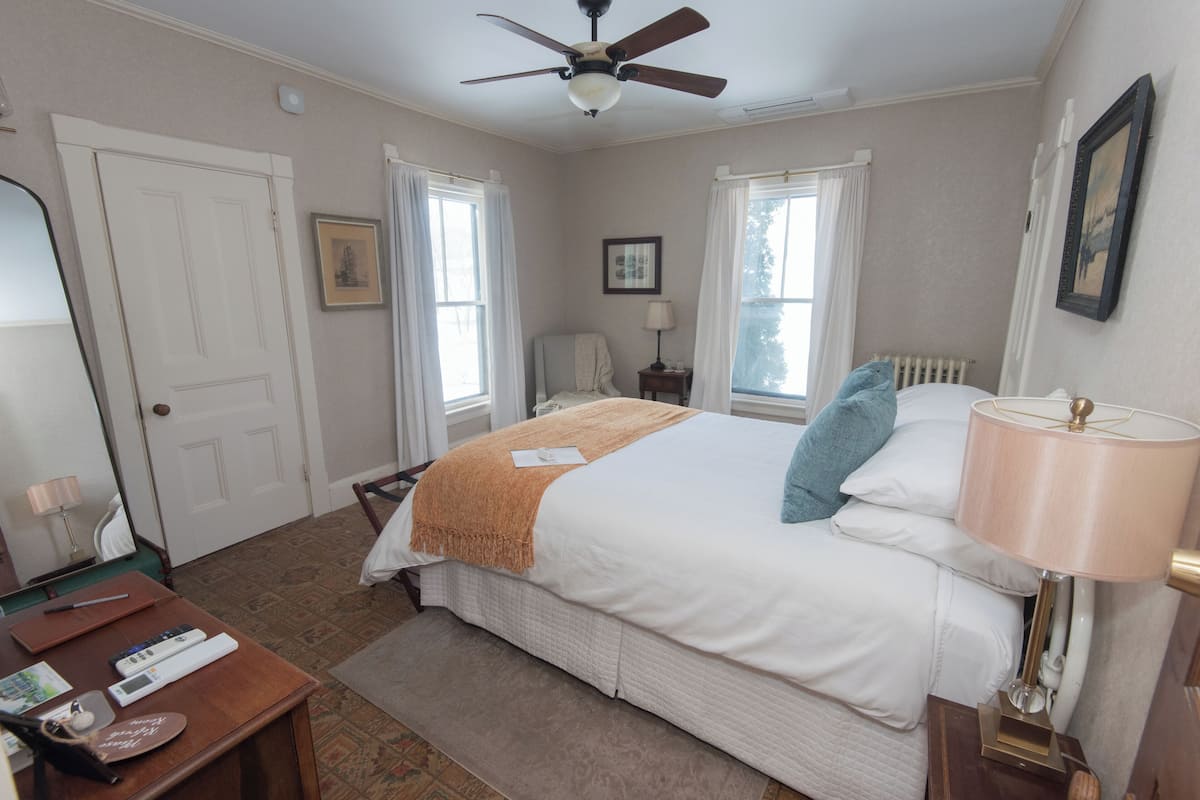 Una habitación de hotel con cama, escritorio, silla, ventilador de techo y ventana con cortinas.