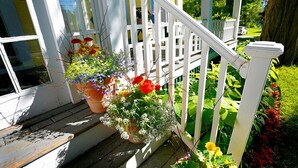 A wooden porch with white railings and potted plants. - The Kendall Inn (Freeport)