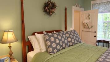 A bedroom with a wooden four-poster bed, green bedding, a nightstand with a lamp, and a wall-mounted floral decoration.
