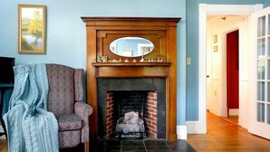 A living room with a fireplace, a patterned armchair, a blue blanket, and a framed picture on the wall. - The Kendall Inn (Freeport)