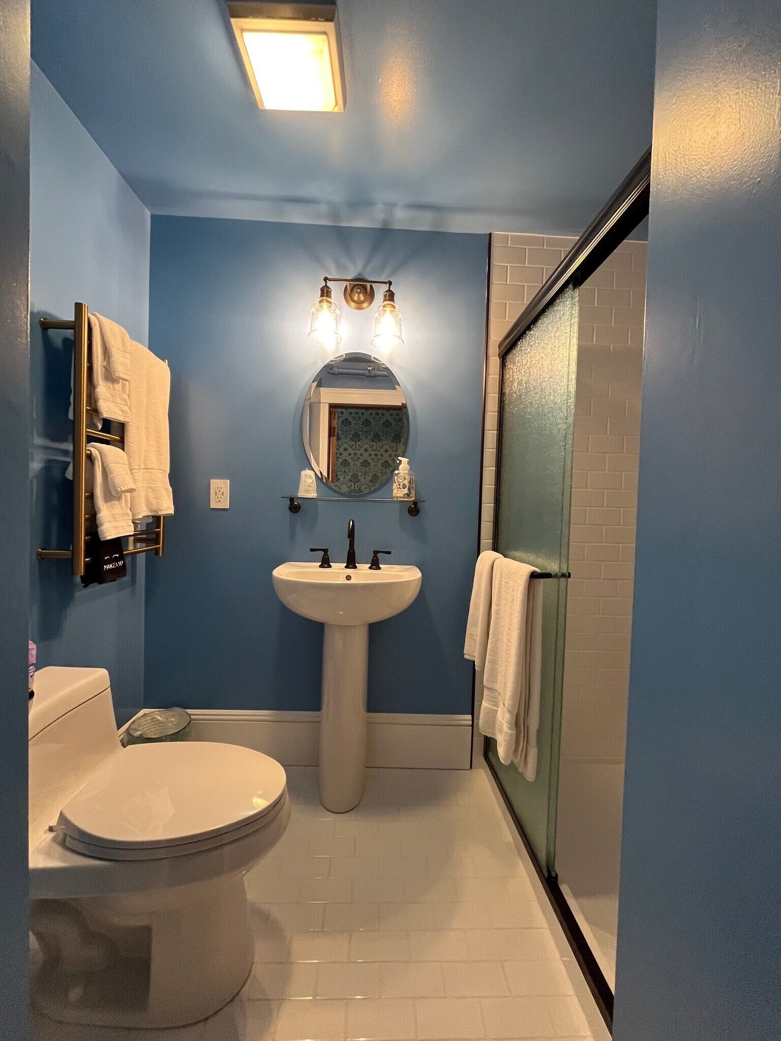 Et badeværelse med et håndvask på fod, toilet, håndklædetørre og et spejl med lys.