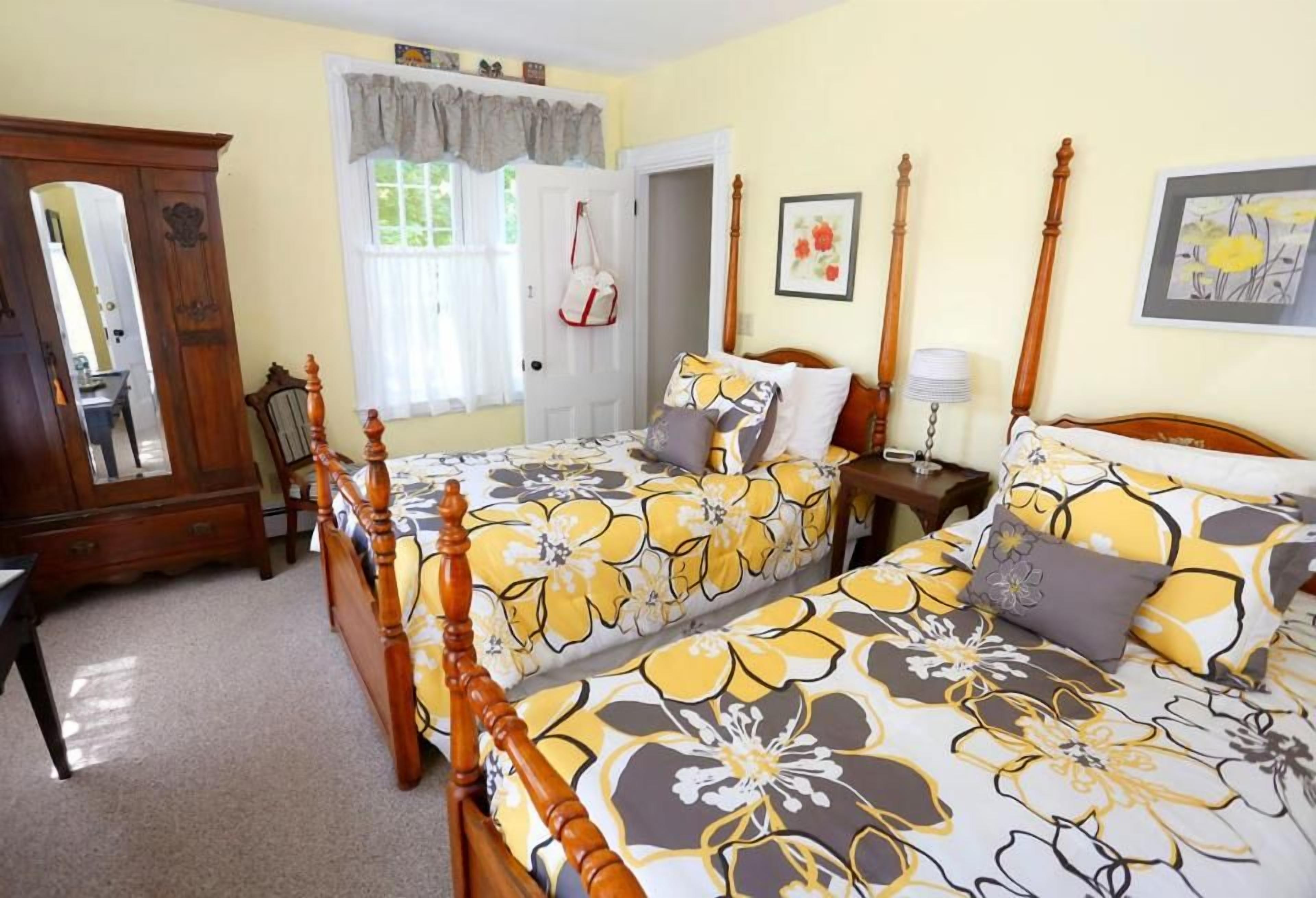 A bedroom with two beds, a wooden wardrobe, a mirror, and a window with curtains.