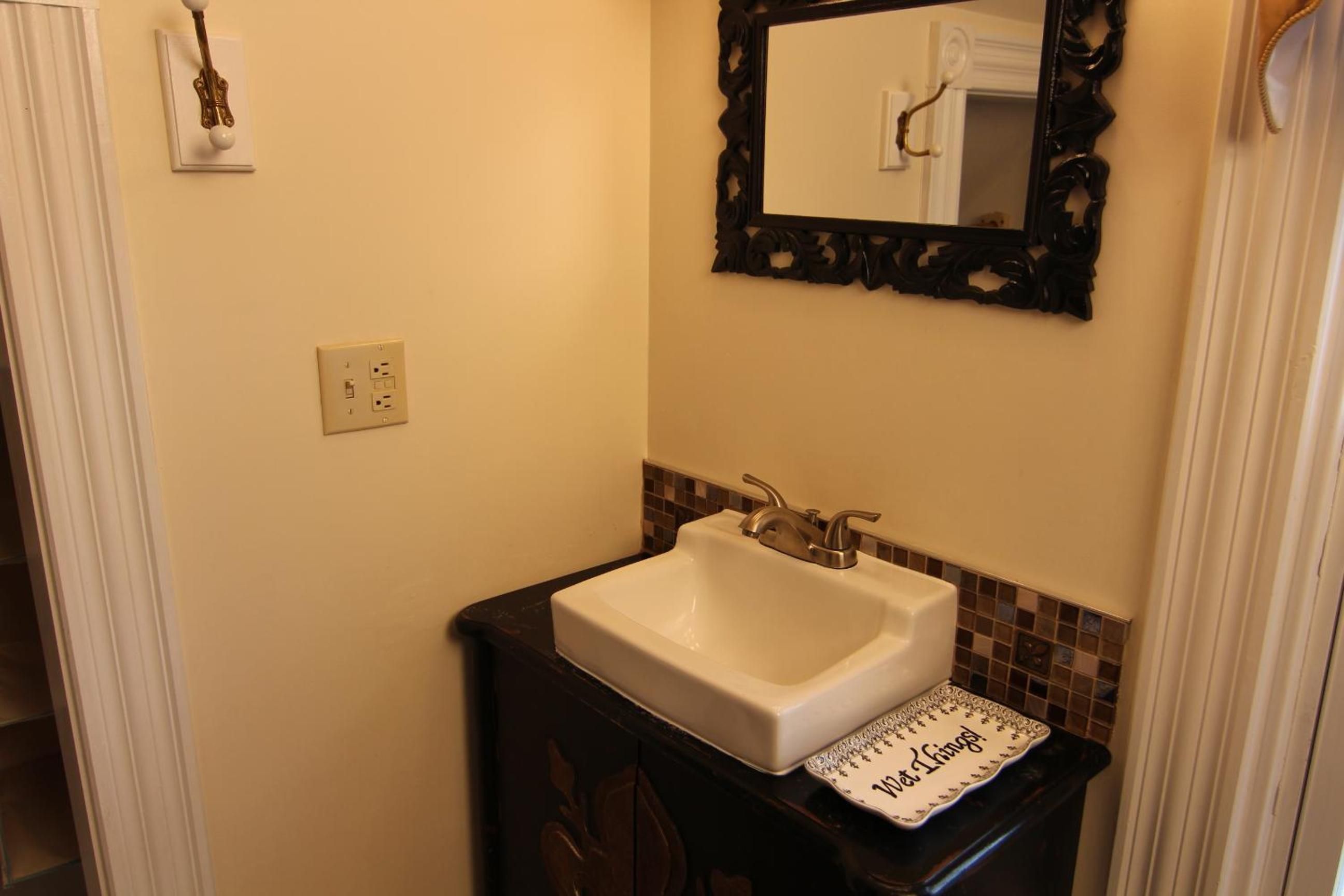 Une salle de bain avec un lavabo blanc, un miroir doté d’un cadre orné et un plateau décoratif sur lequel on peut lire les mots « Over It King ! ».