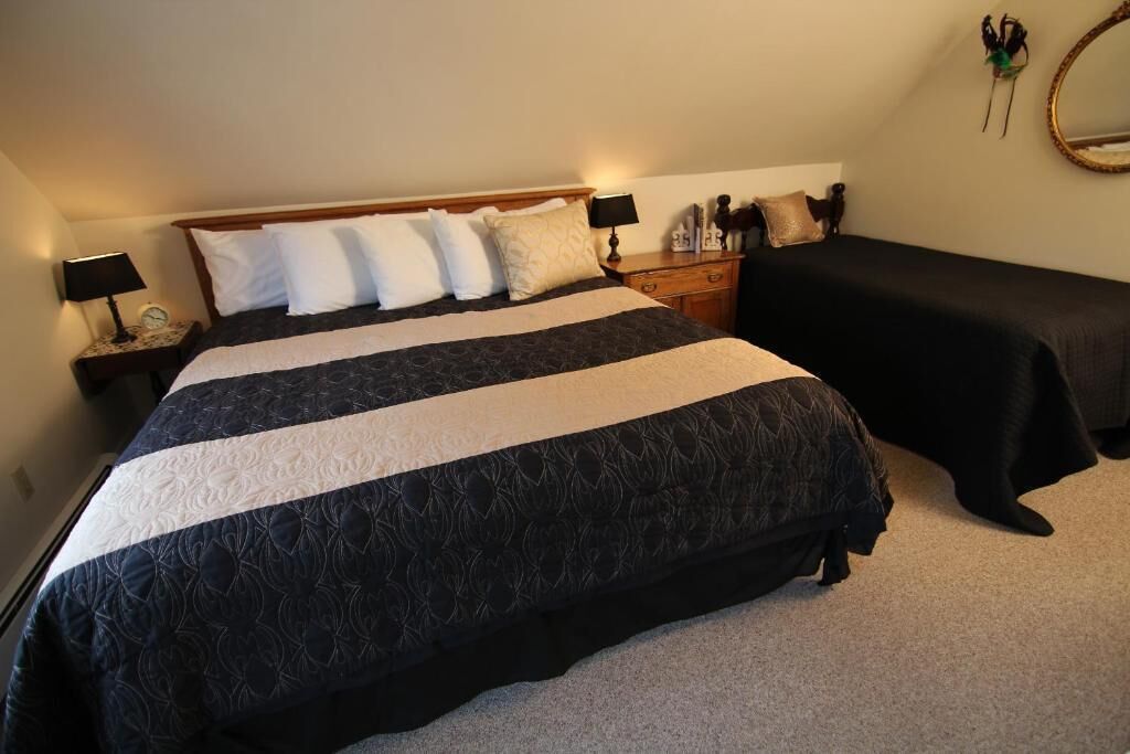 A bedroom with a large bed, bedside tables with lamps, a dresser, a mirror, and a small bedside table with decorative items.