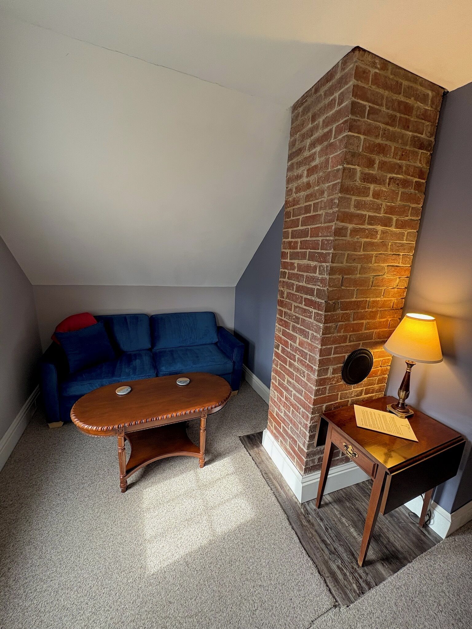 Une pièce chaleureuse avec un canapé bleu, une table basse en bois, un mur décoratif en briques et une lampe sur une table d’appoint.
