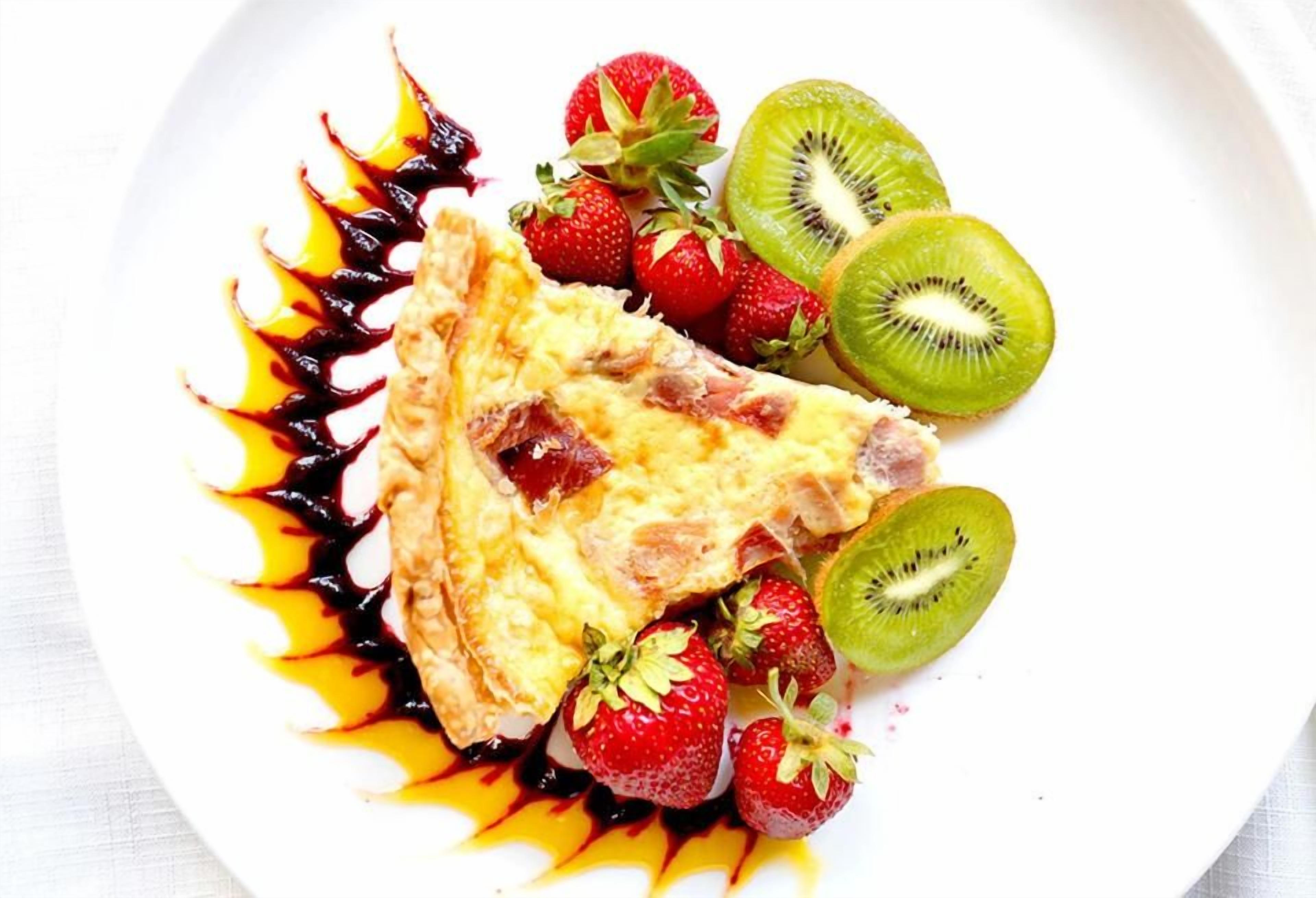 A plate with a slice of quiche, strawberries, and kiwi slices.