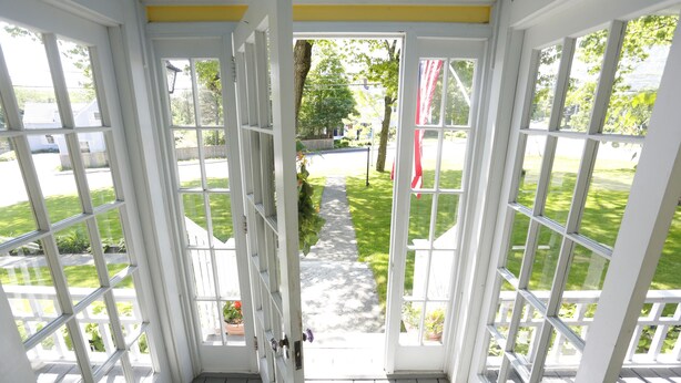 A covered porch with white railings and a view of a well-maintained lawn and pathway. - The Kendall Inn (Freeport)