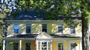 A two-story yellow house with a front porch, a flag, and a well-maintained garden. - The Kendall Inn (Freeport)