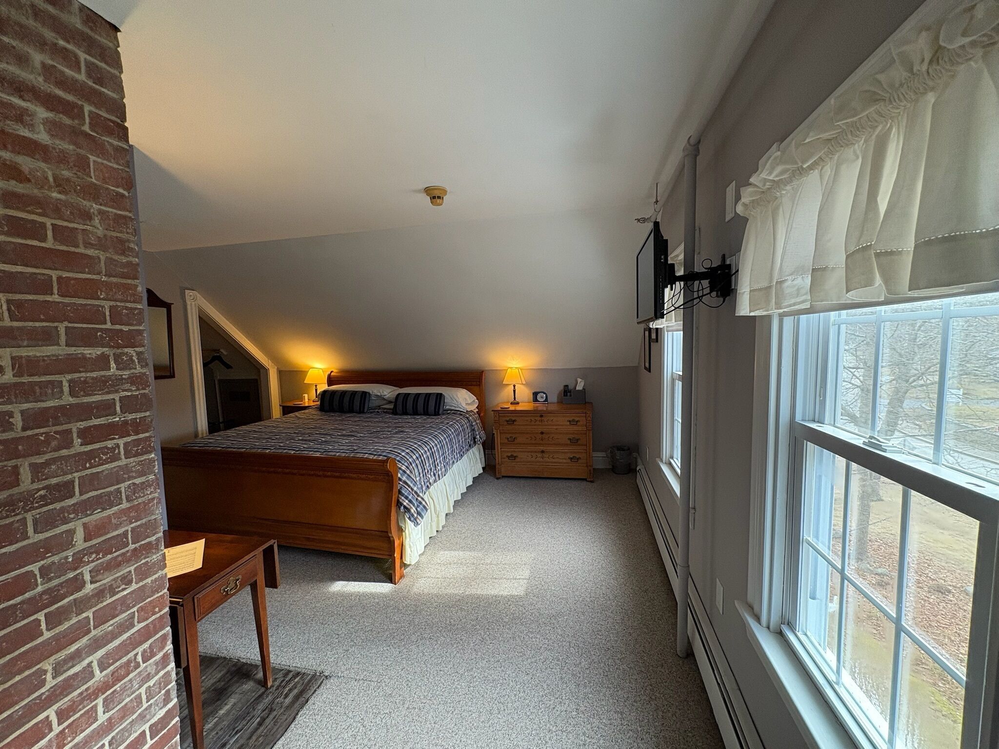 Ein Schlafzimmer mit einem großen Bett, einem Schminktisch, einem Nachttisch und einem Fenster mit Vorhängen.
