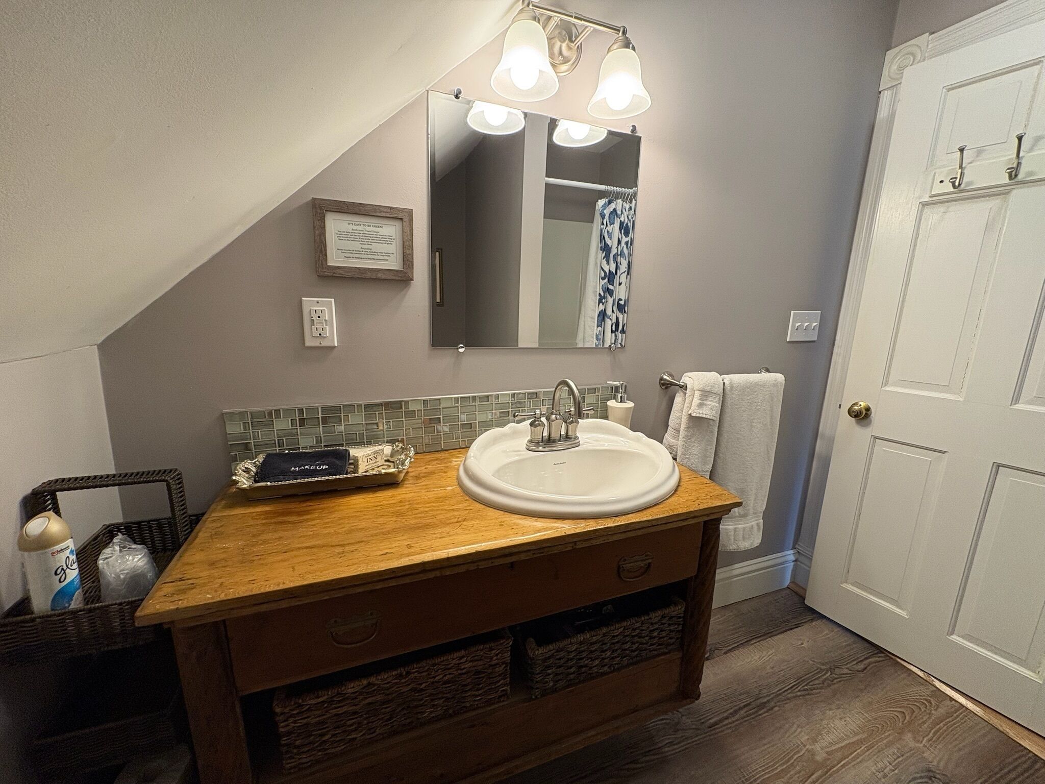 Un bagno con un mobile lavabo in legno, un lavandino bianco, uno specchio con luci, un porta asciugamani e una porta.
