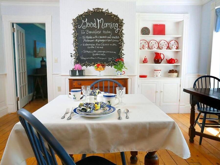 Uma sala de jantar com uma mesa posta para o café da manhã, um cardápio em lousa e um armário branco com louças.