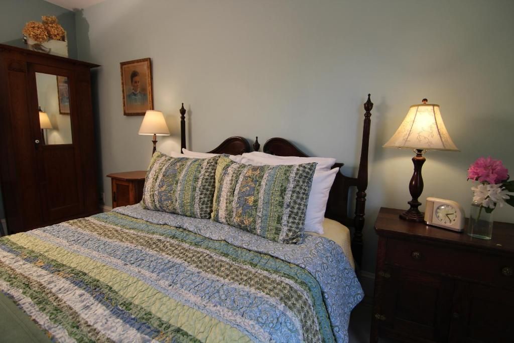 A bedroom with a four-poster bed, a bedside table with a lamp, a clock, and a mirror.