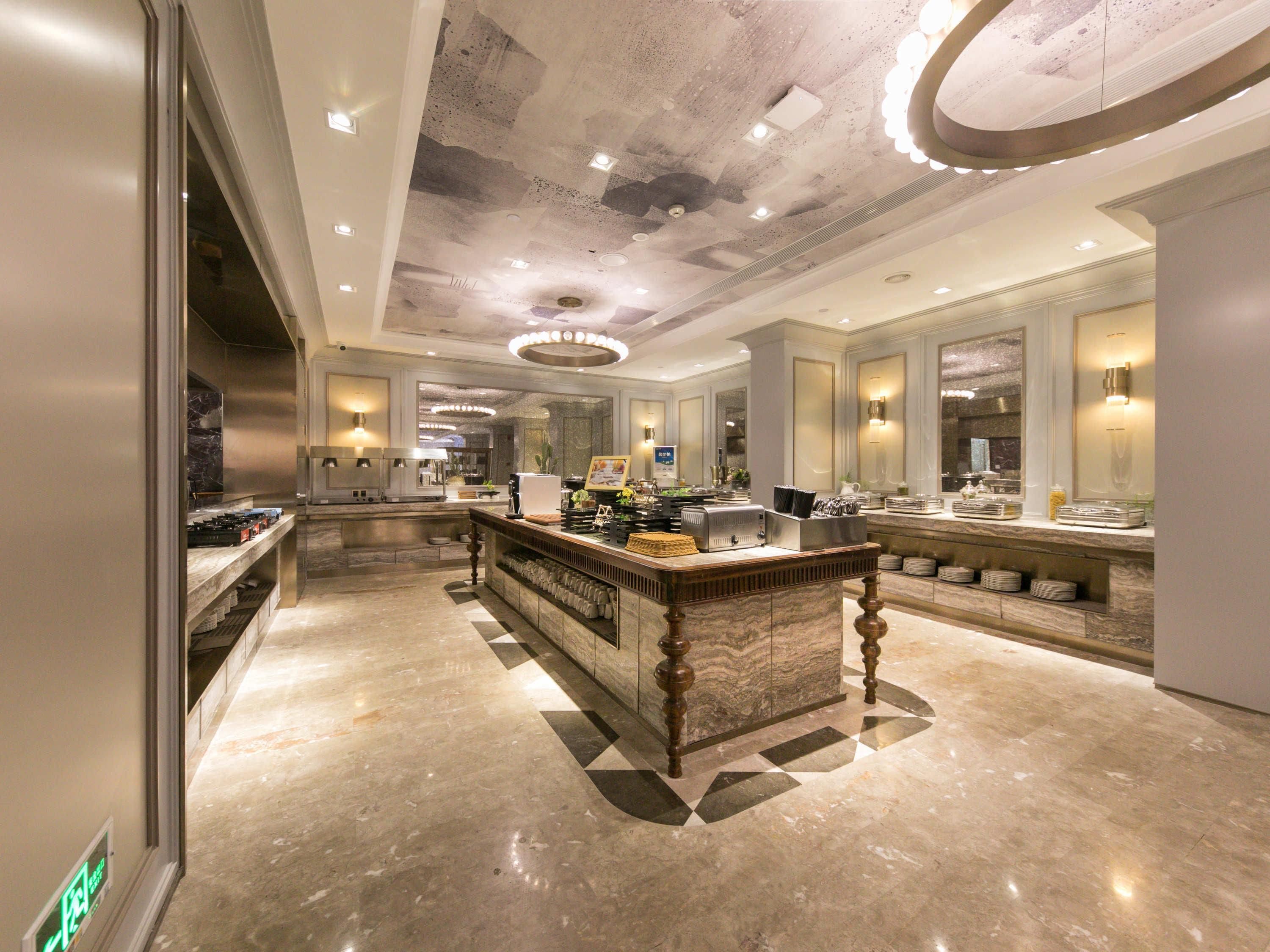 A spacious hotel lobby with a marble floor, a central bar area, and a modern ceiling design.