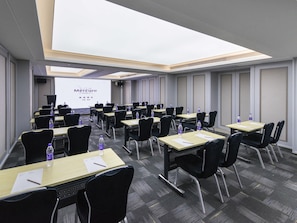 Un salón de conferencias con filas de mesas, sillas y una pantalla de proyección mostrando 'Mercure Hotels'.
