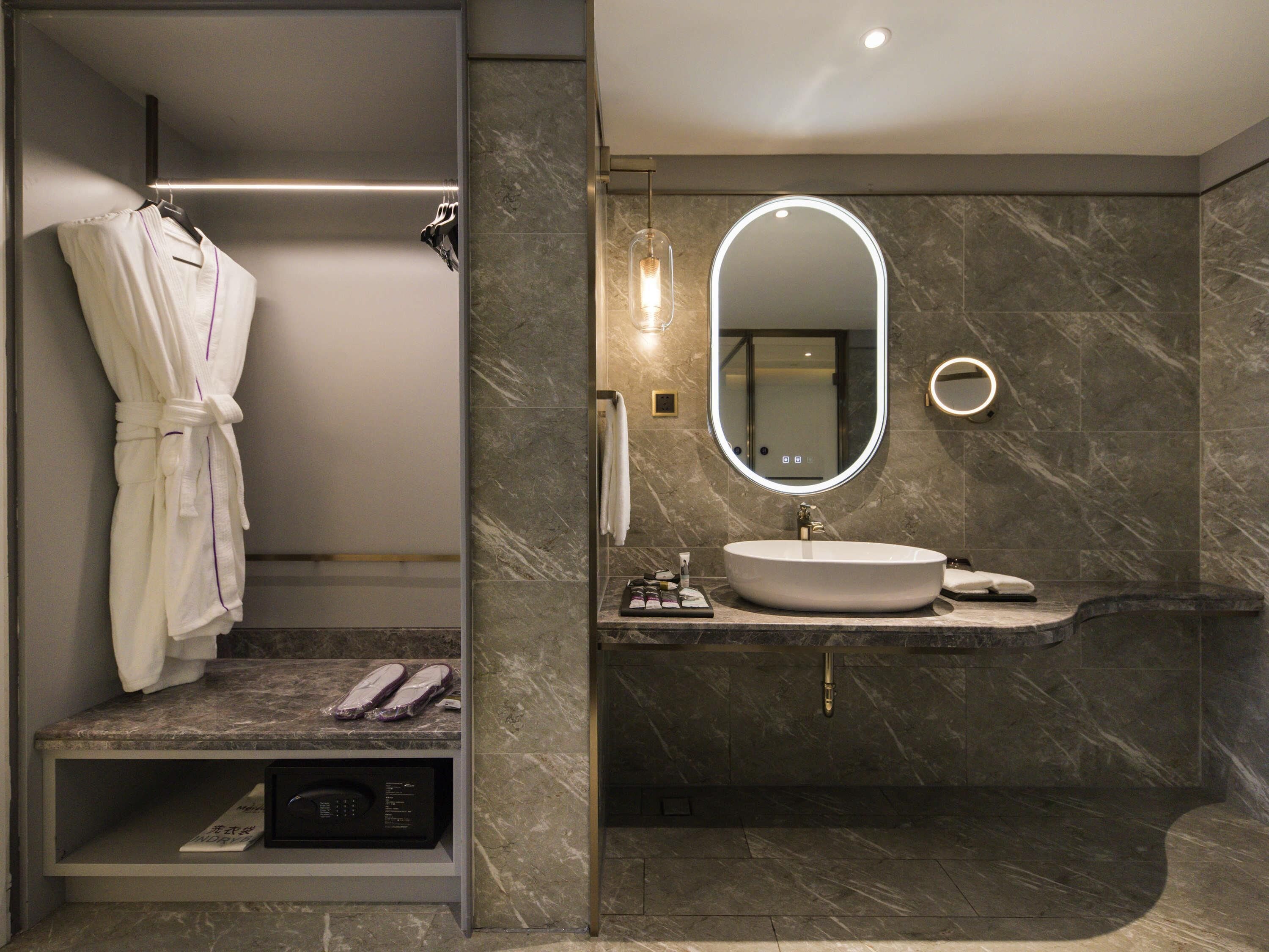 Un baño moderno con lavamanos de mármol, un espejo grande y una bata colgada en un perchero.
