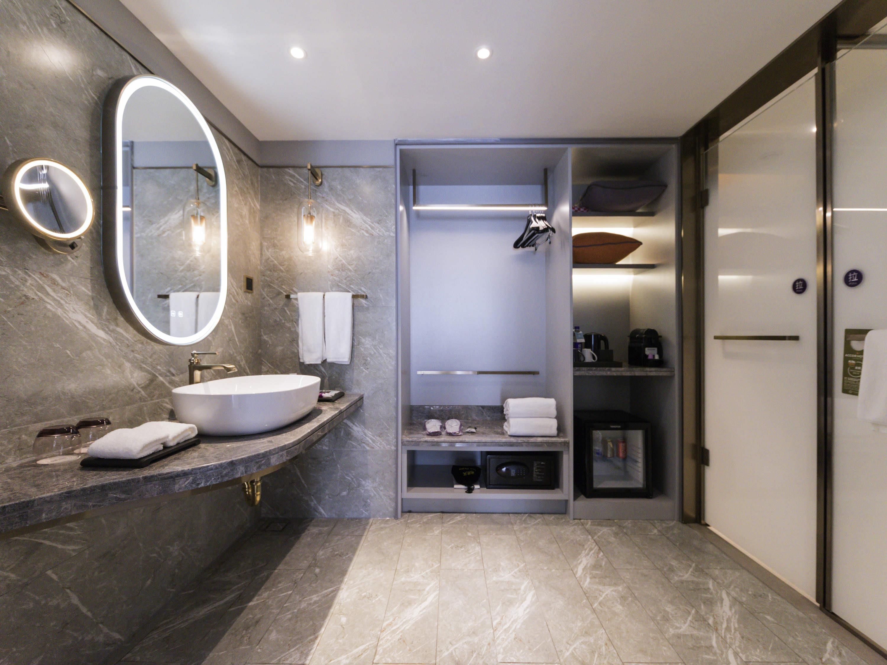 A modern bathroom with a large oval mirror, a round sink, and a built-in shower area.
