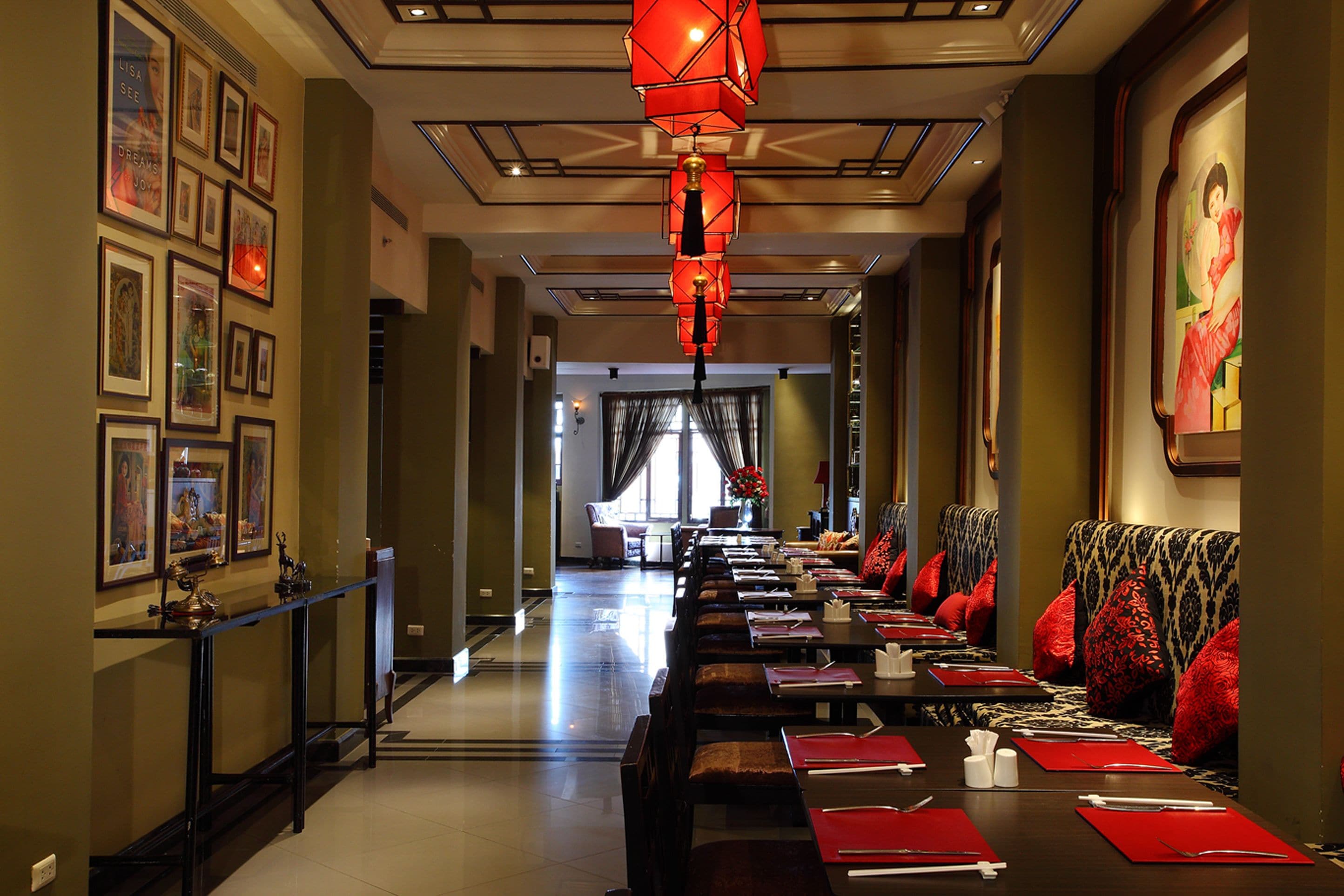A hotel lobby with a long reception desk, seating area with red cushions, framed artwork on the walls, and a large painting on the right.