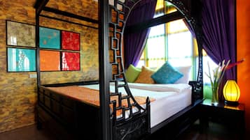 A four-poster bed with a wooden frame, a white mattress, and colorful pillows. There is a window with purple curtains and a vase with flowers on a nightstand beside the bed.