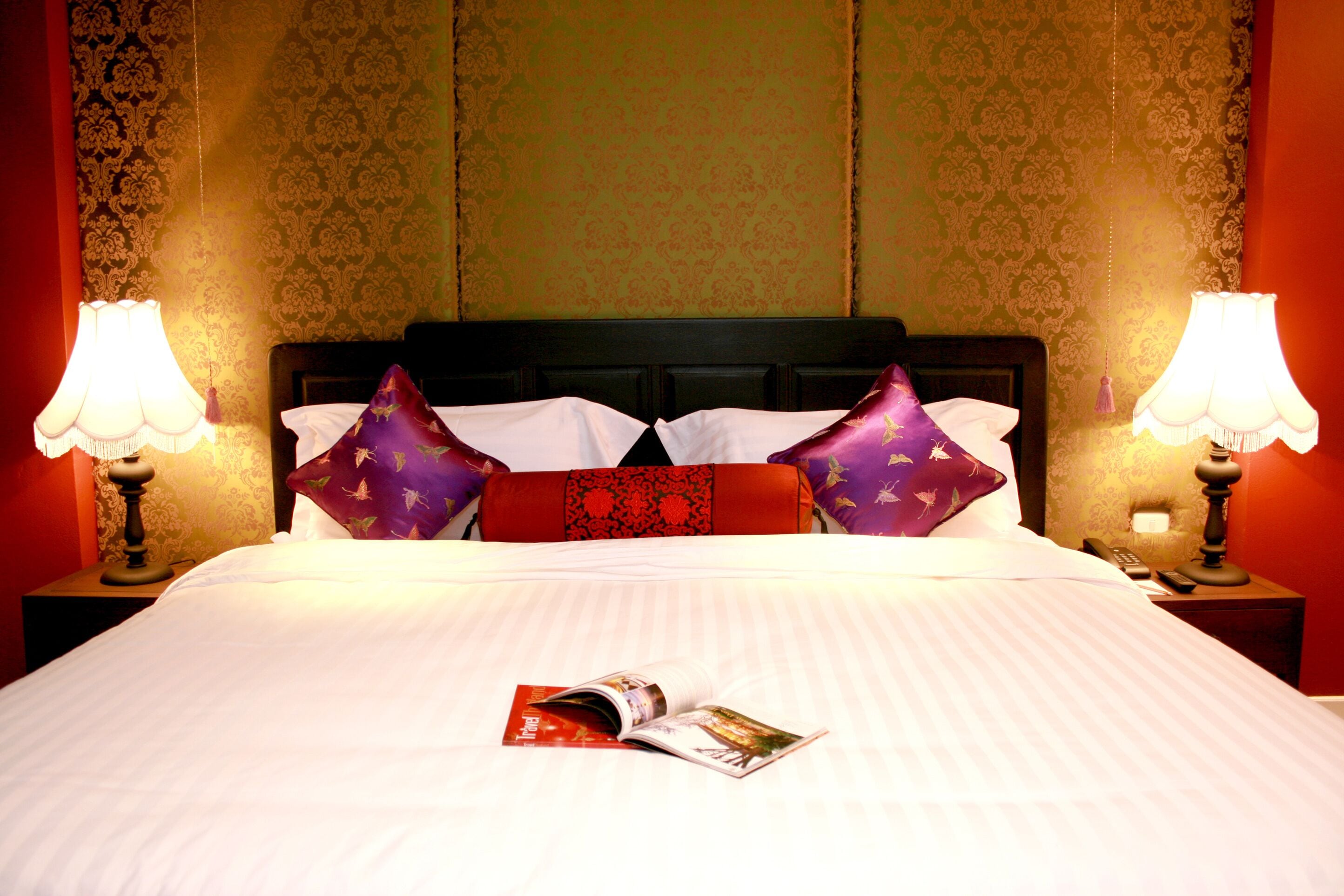 A neatly made bed with a magazine, two lamps, and patterned pillows.