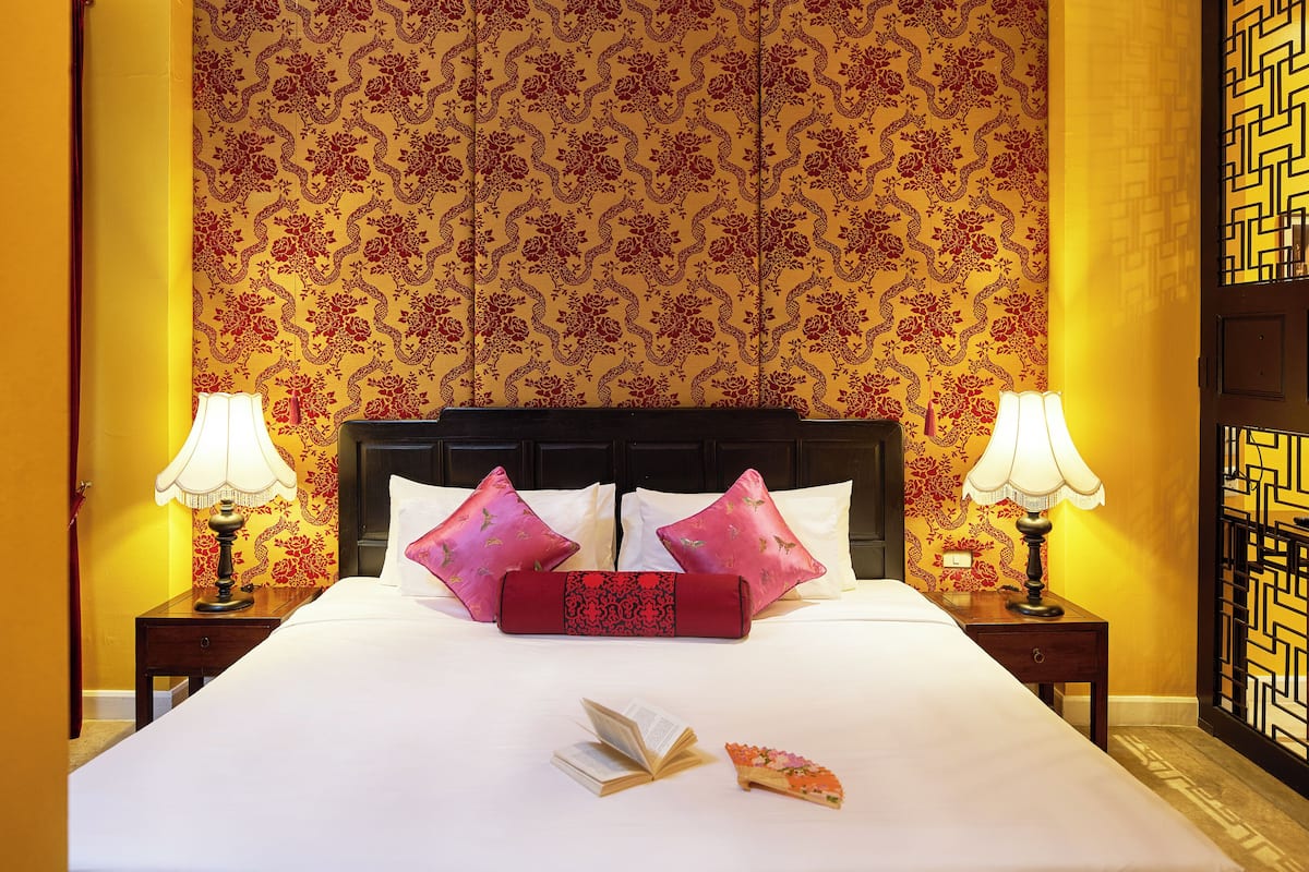 Quarto de hotel com uma cama grande, duas mesas de cabeceira com abajures, uma almofada decorativa, um livro e uma pizza na cama.