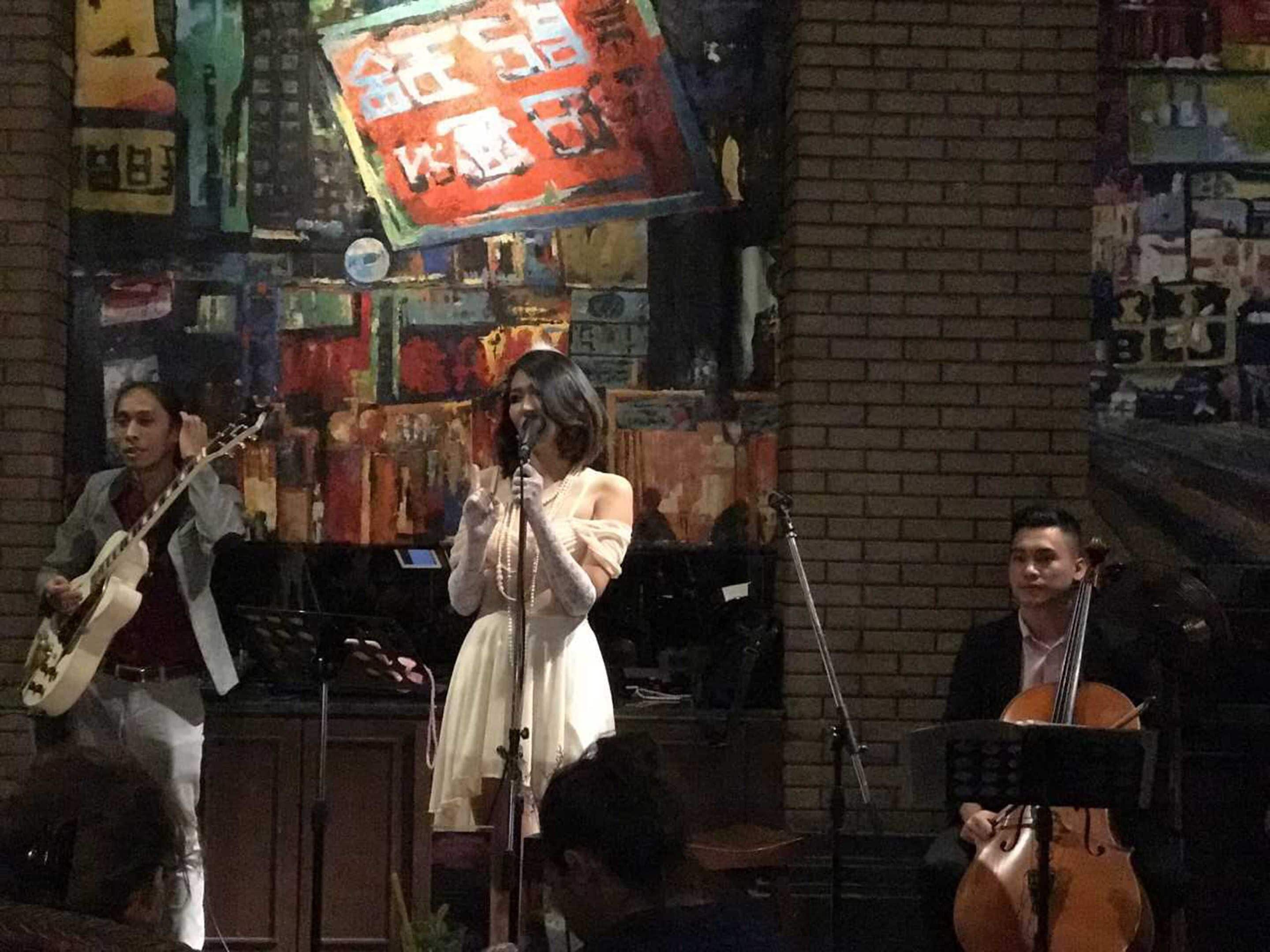 Een band treedt op op een podium, met bakstenen muren en kleurrijke posters op de achtergrond.