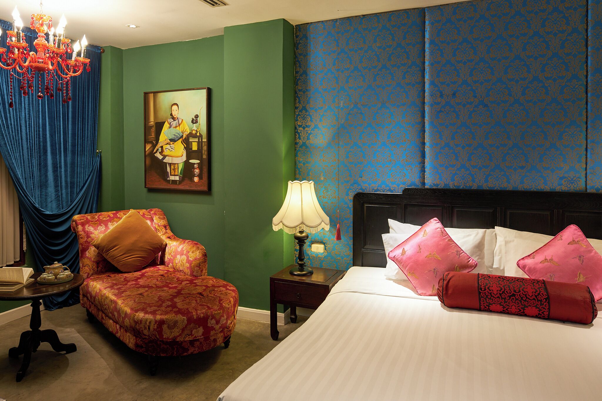 A hotel room with a bed, a chair, a nightstand, a lamp, and a painting on the wall.