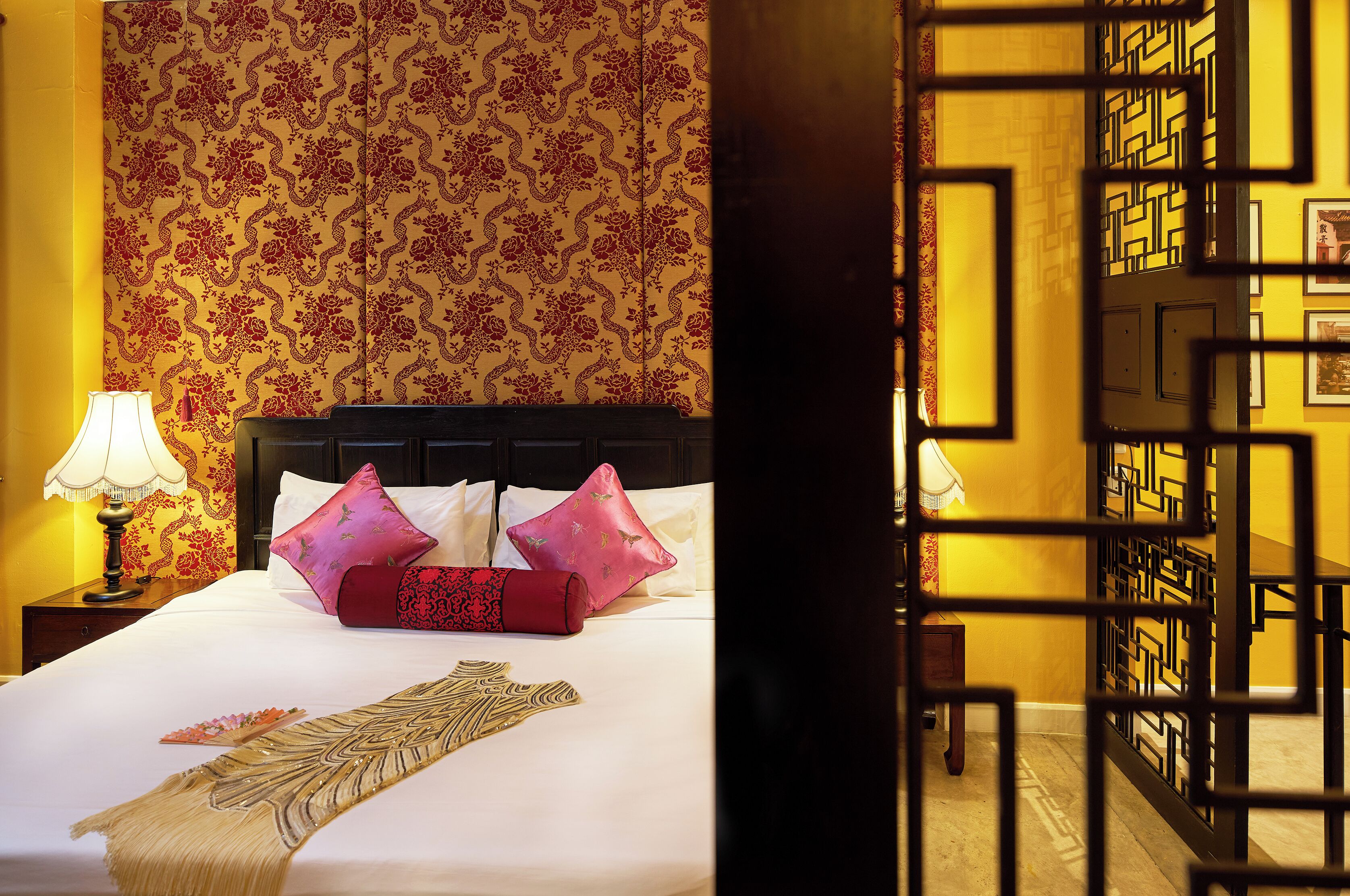 A hotel room with a bed, pillows, a lamp, and a patterned wall.