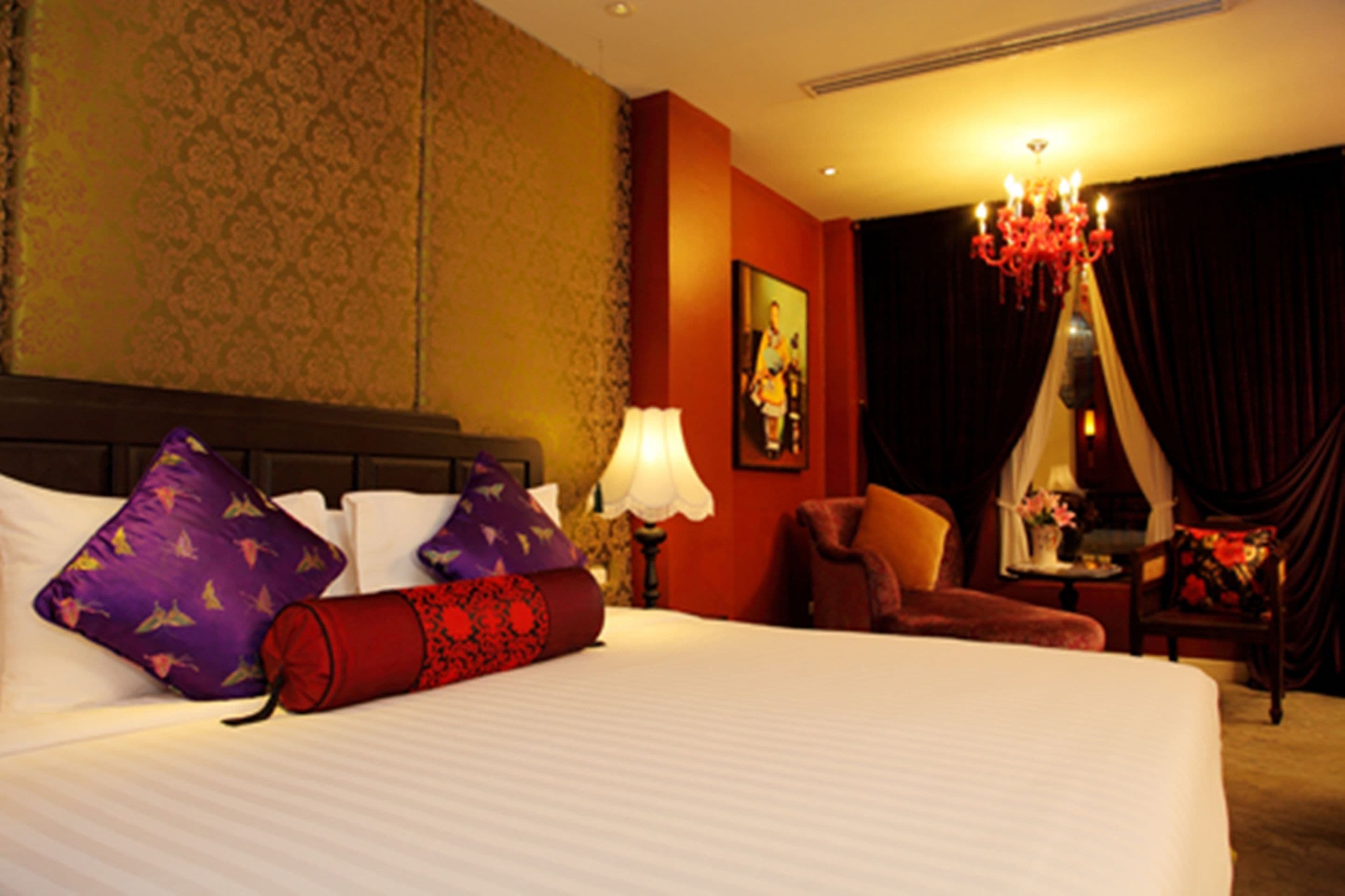 A hotel room with a large bed, a chandelier, a chair, and a painting on the wall.