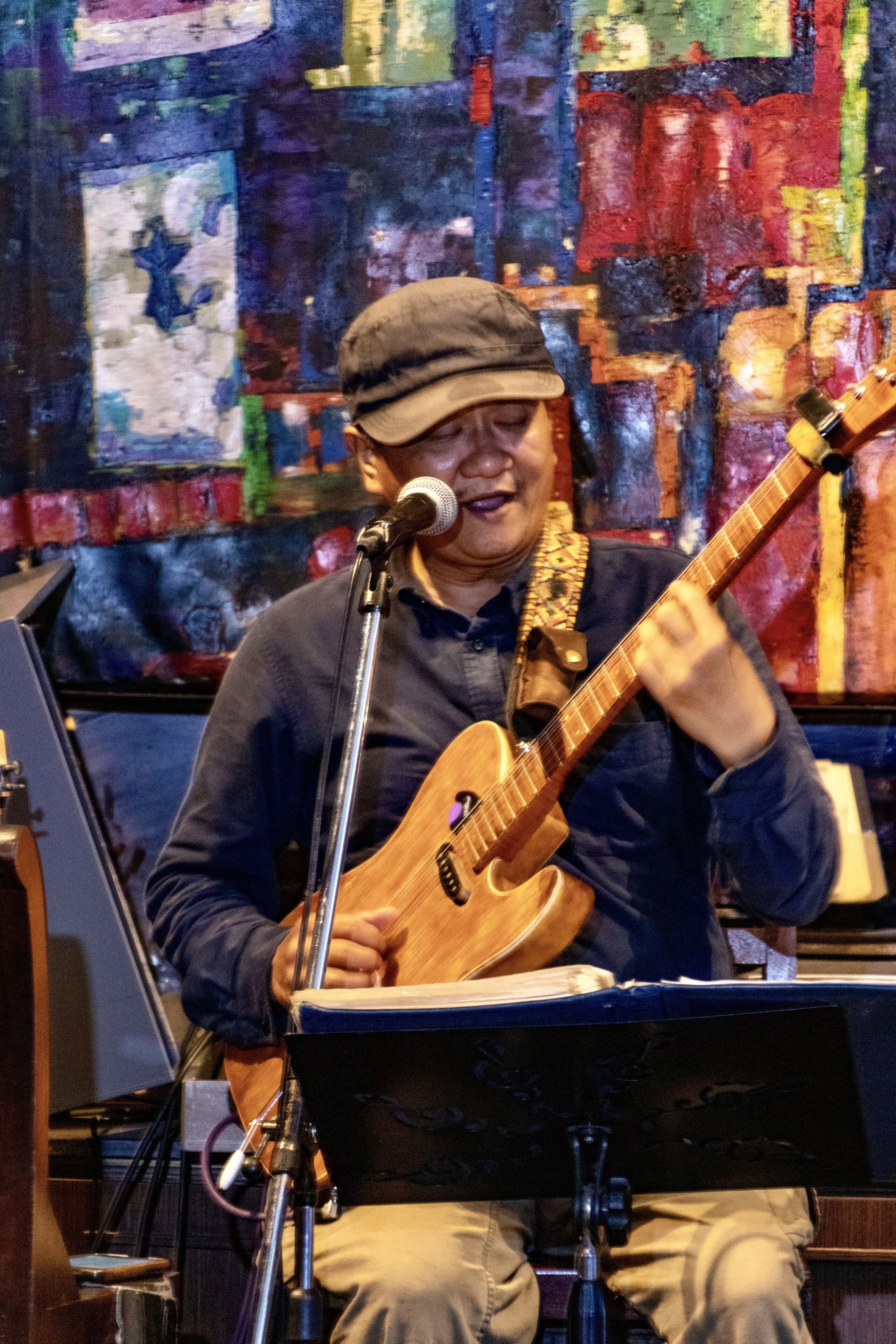 A person playing a guitar on a stage with a microphone and music stand.