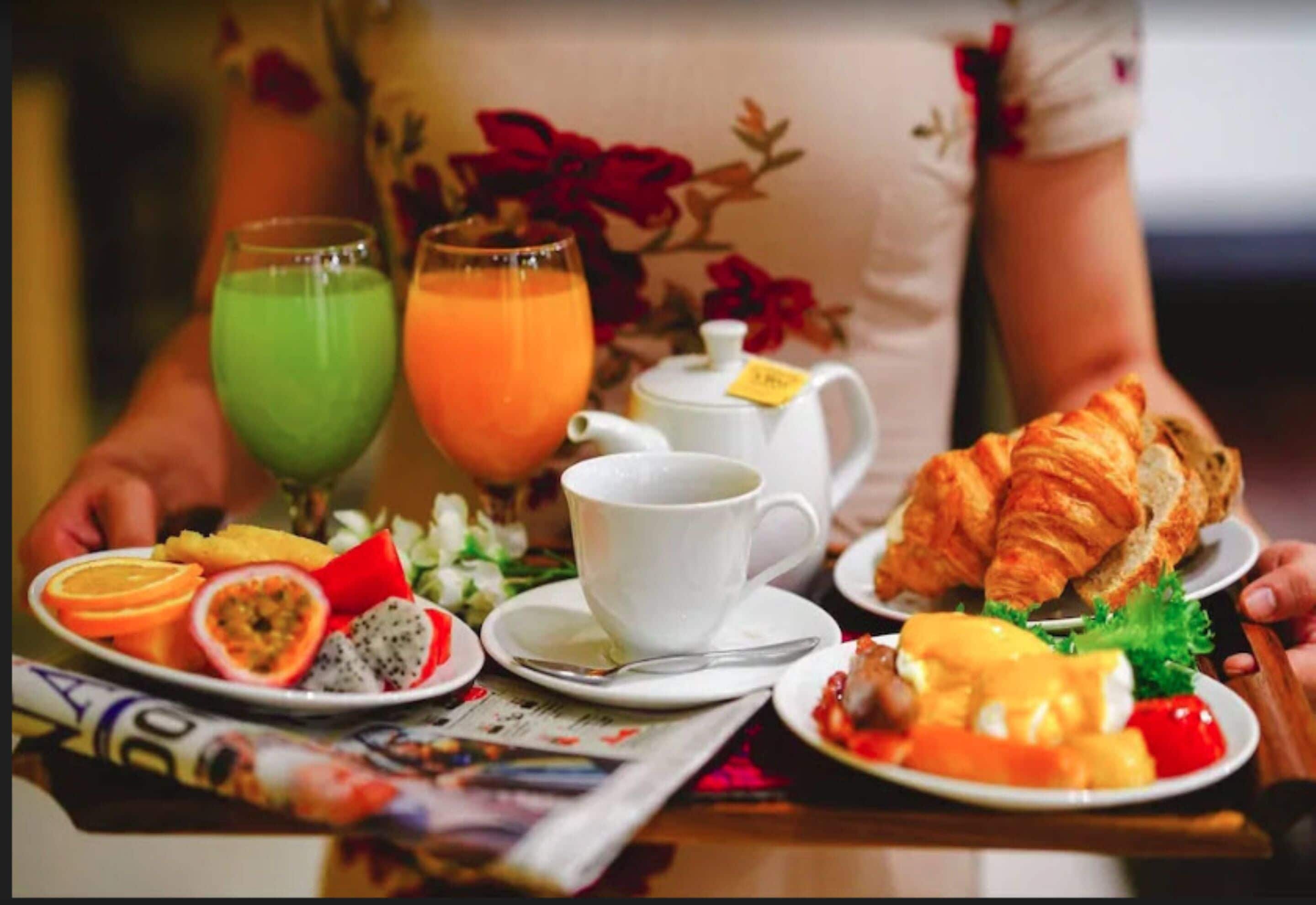 A breakfast setting with a croissant, orange slices, passion fruit, and a green drink on a table.