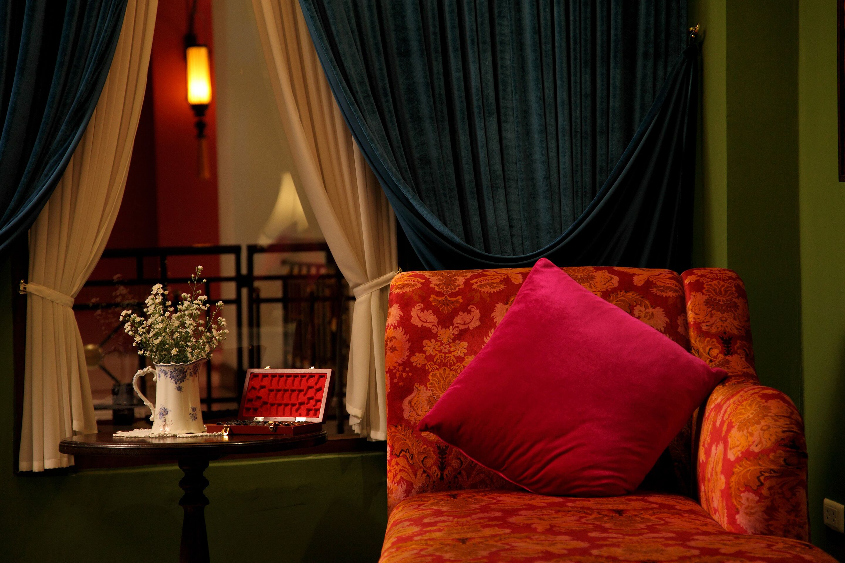 A room with a sofa, a vase with flowers, and curtains.