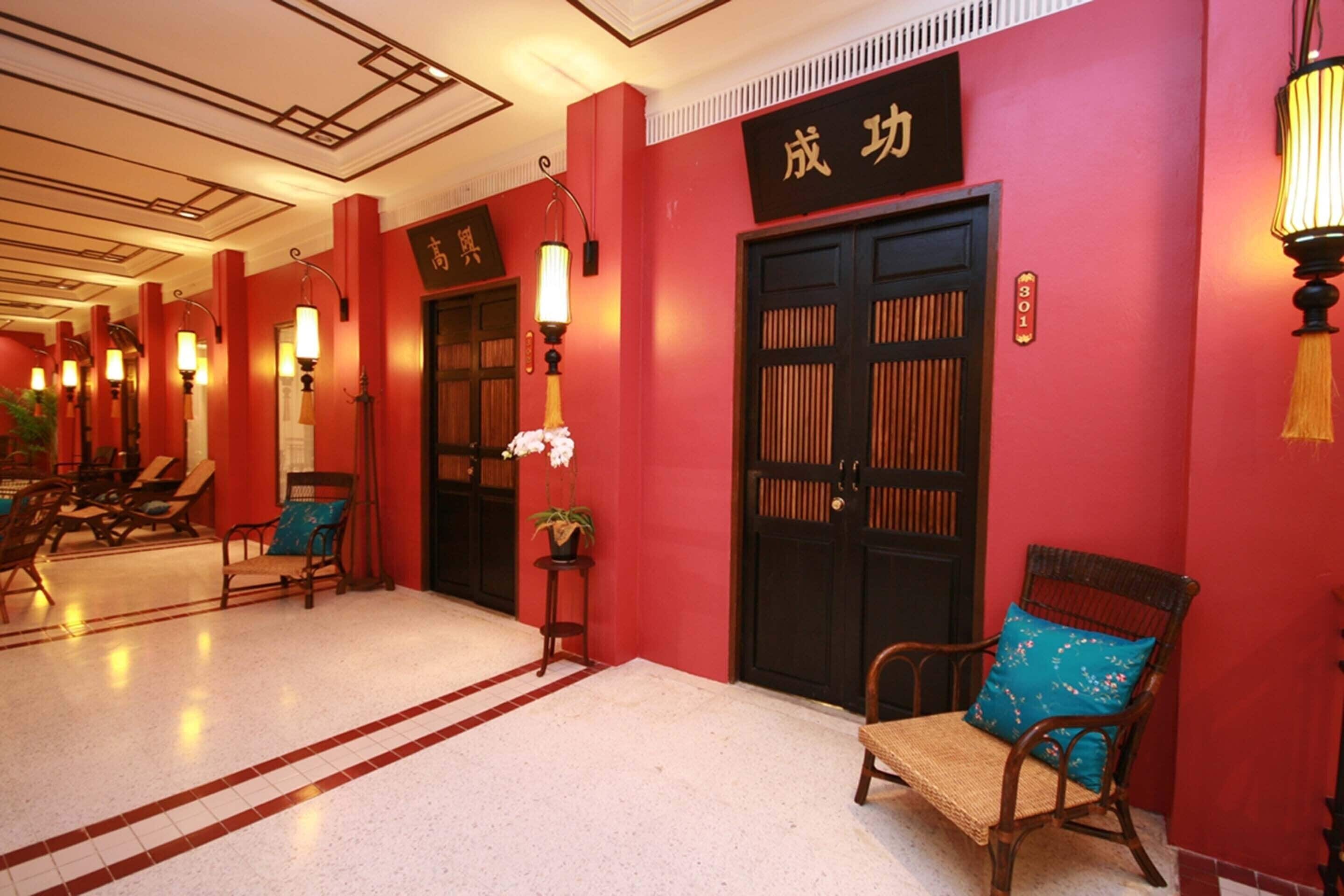 Un hall d’hôtel aux murs rouges, doté de portes de style chinois traditionnel et d’espaces aménagés pour s’asseoir.