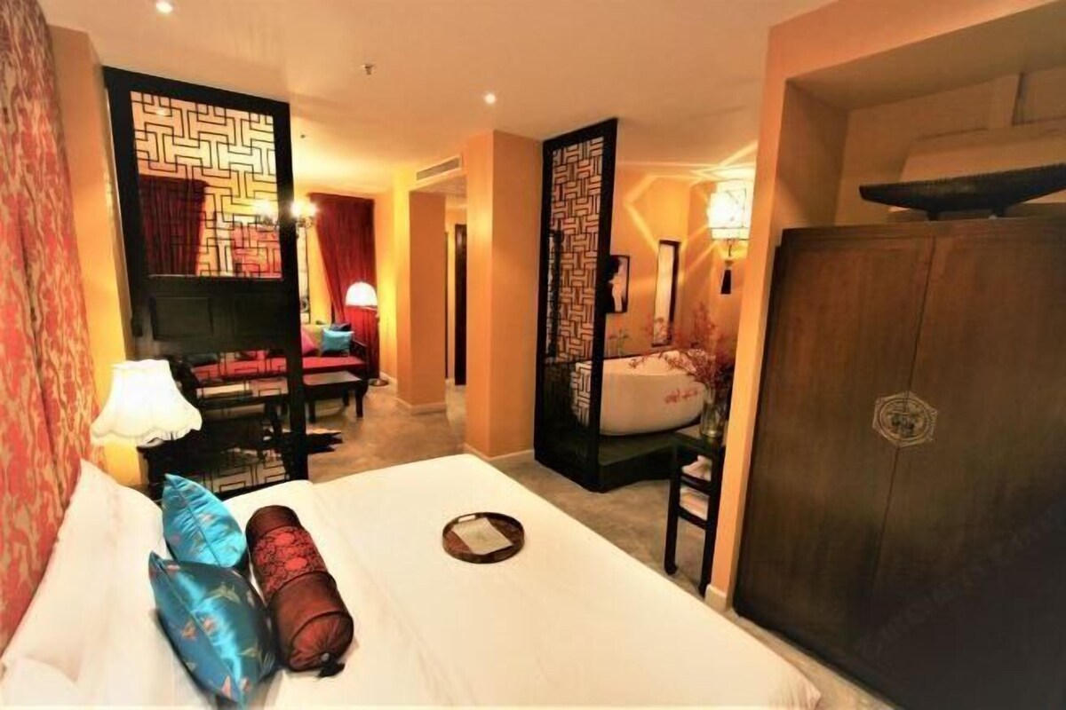 A hotel room with a bed, a desk, a chair, a wardrobe, and a decorative screen.