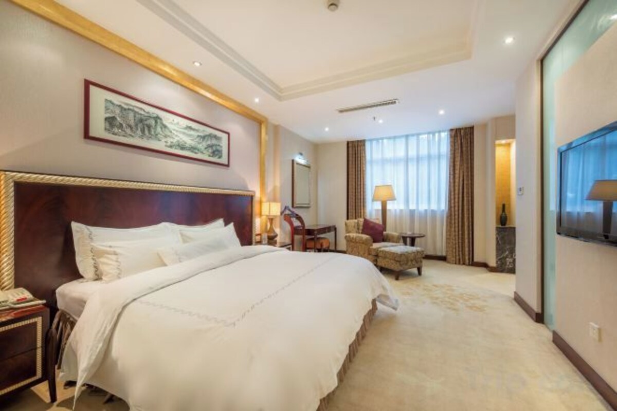 A hotel room with a large bed, a desk, a chair, a TV, and a window with curtains.