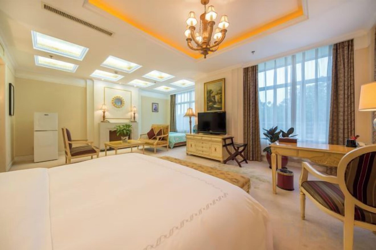 A hotel room with a large bed, a desk, a television, and a seating area.