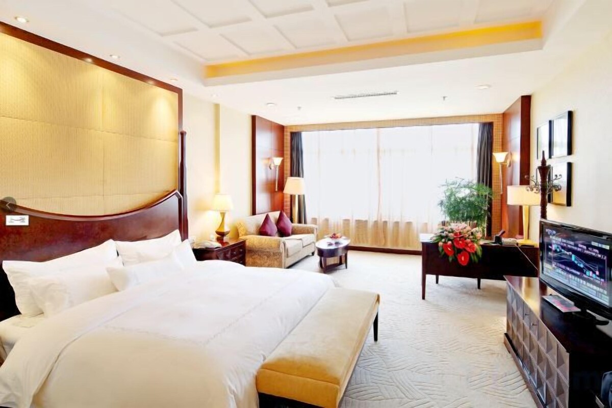 A hotel room with a large bed, a television, a desk, and a sofa.