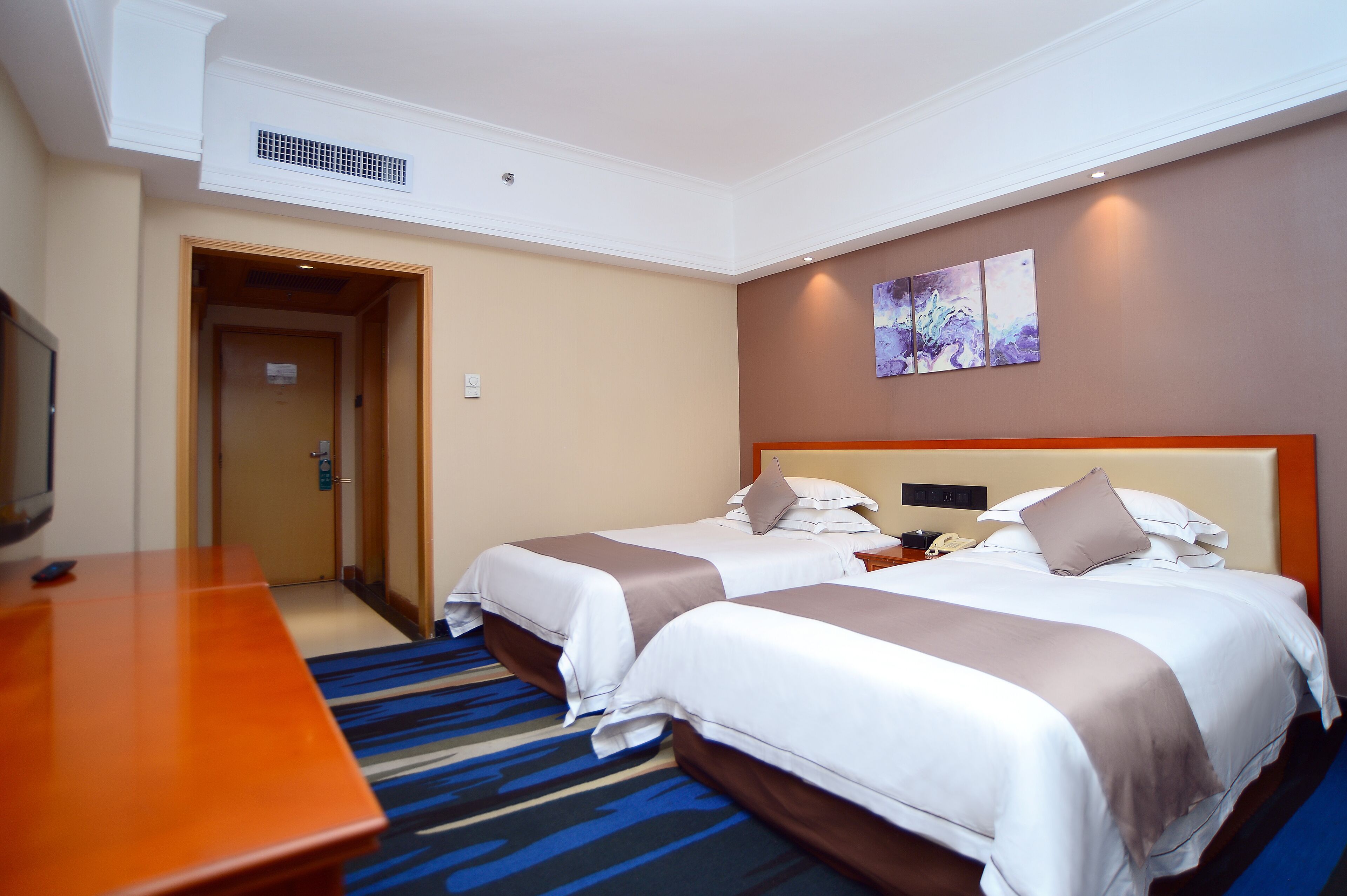A hotel room with two beds, a wooden desk, and a television.