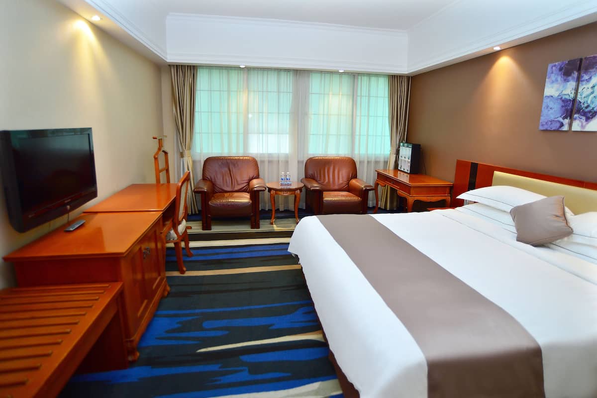 A hotel room with a bed, two armchairs, a TV, a desk, and a small table.