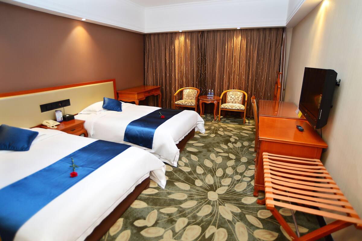 A hotel room with two beds, a TV, a desk, and a chair.