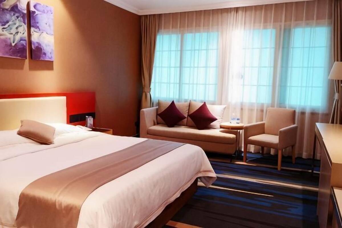 A hotel room with a large bed, a sofa, a chair, a small table, and a desk.