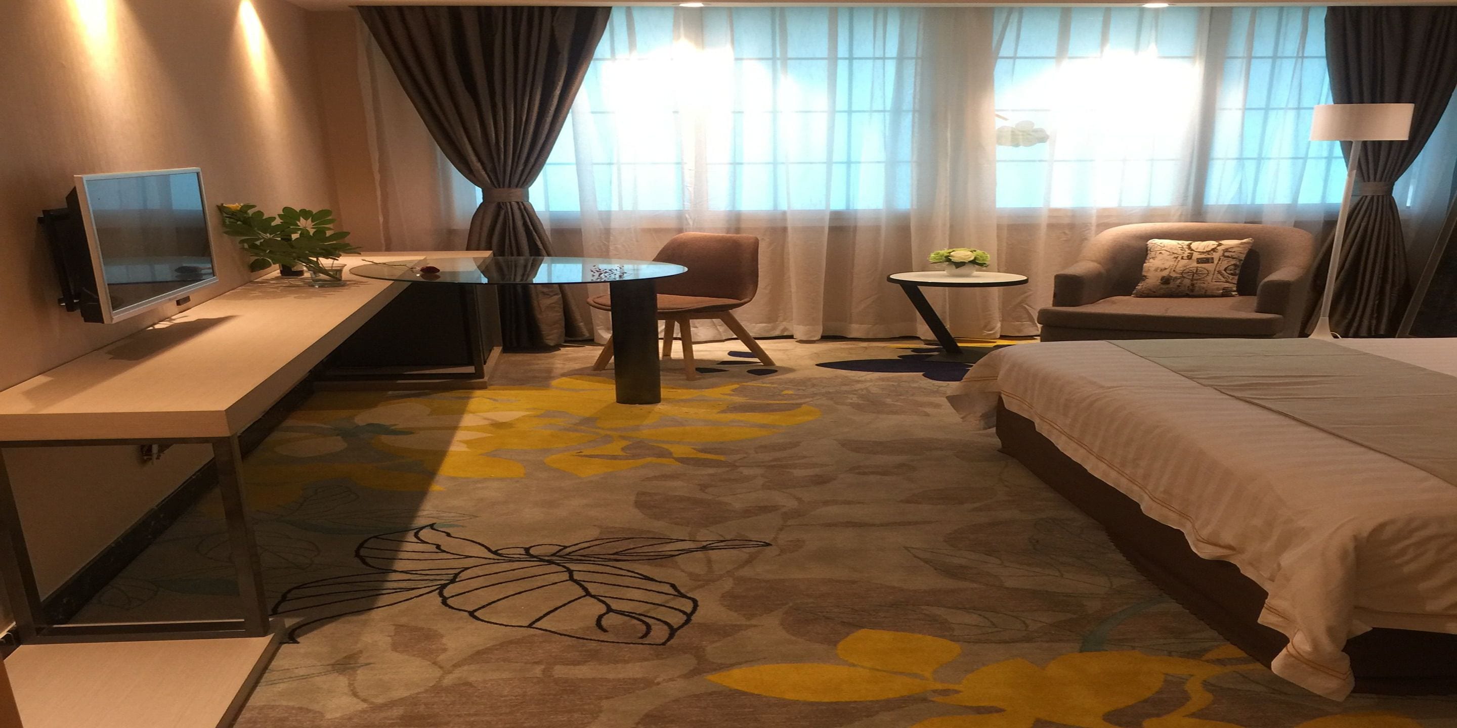 A hotel room with a bed, a desk with a monitor, a chair, a small table, and a sofa.