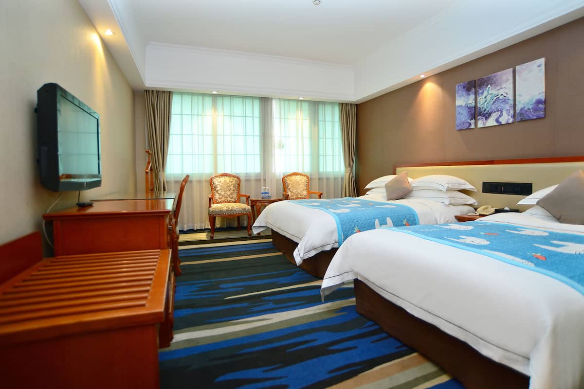 A hotel room with two beds, a desk, a TV, and a chair.