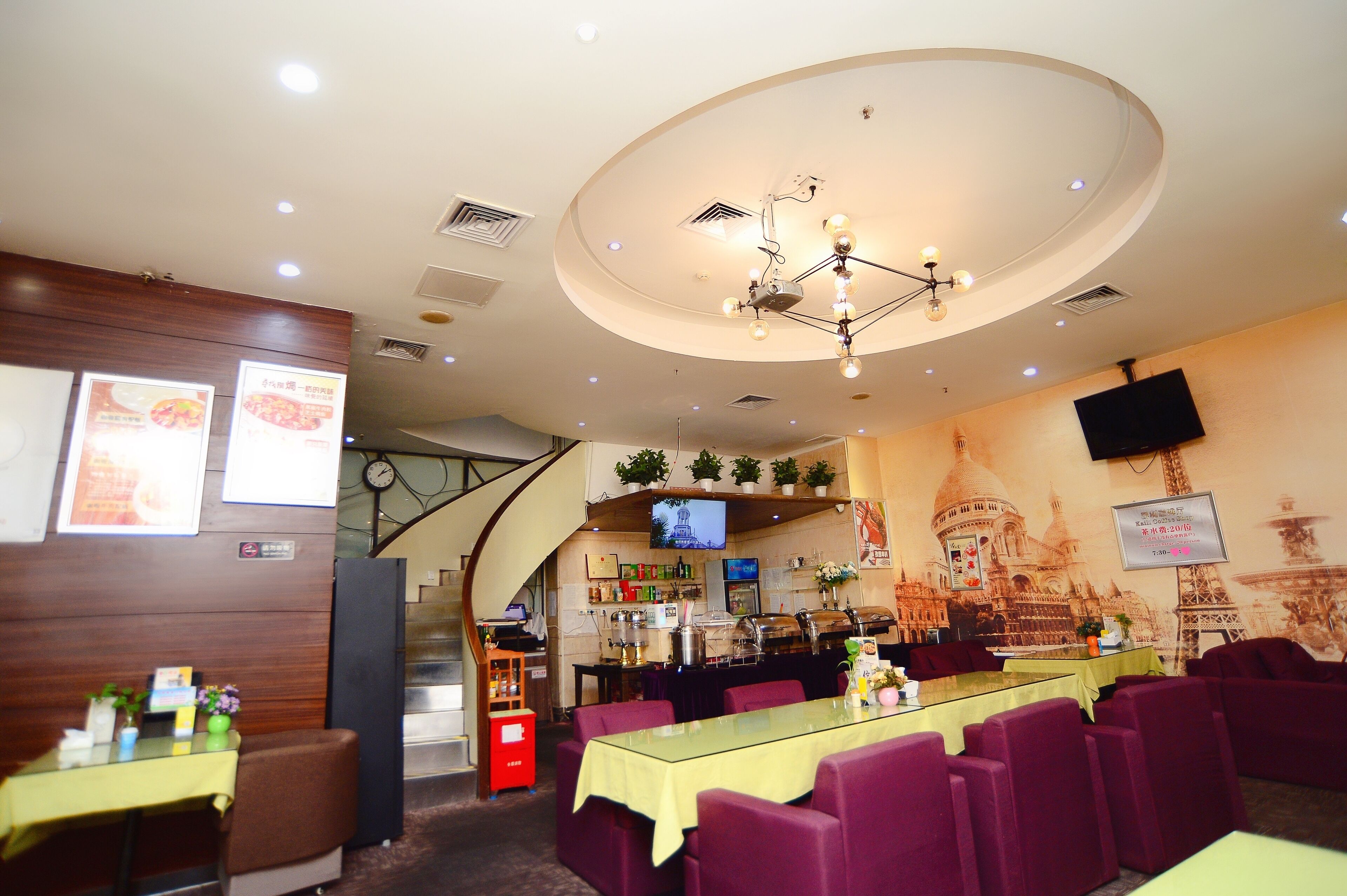 A restaurant with a long table, purple chairs, a chandelier, a TV, and a wall with a cityscape mural.