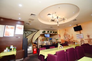 A restaurant with a long table, purple chairs, a chandelier, a TV, and a wall with a cityscape mural. - Shenzhen Kaili Hotel (Shenzhen)
