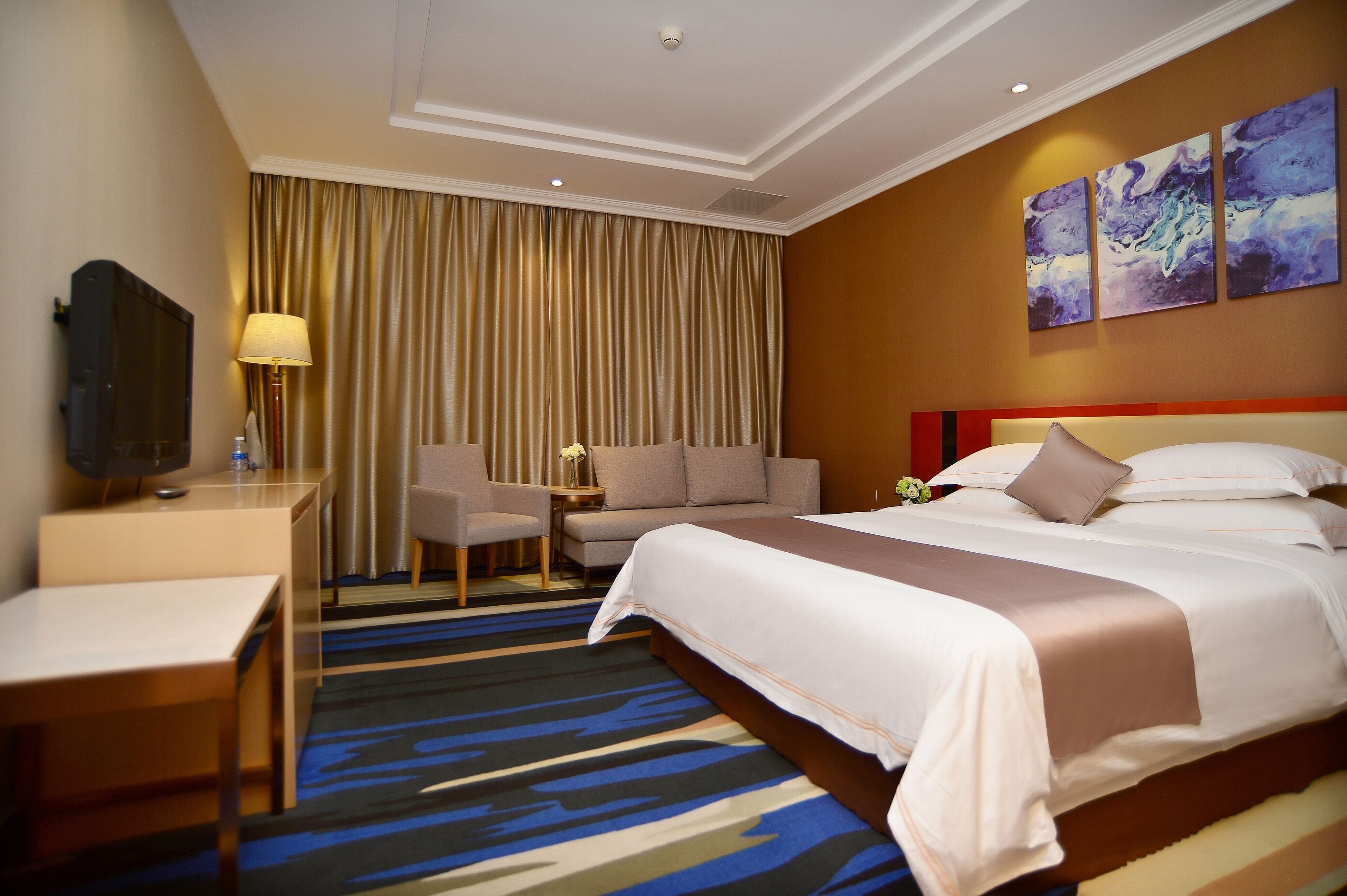 A hotel room with a large bed, a desk, a chair, a TV, and a curtain.