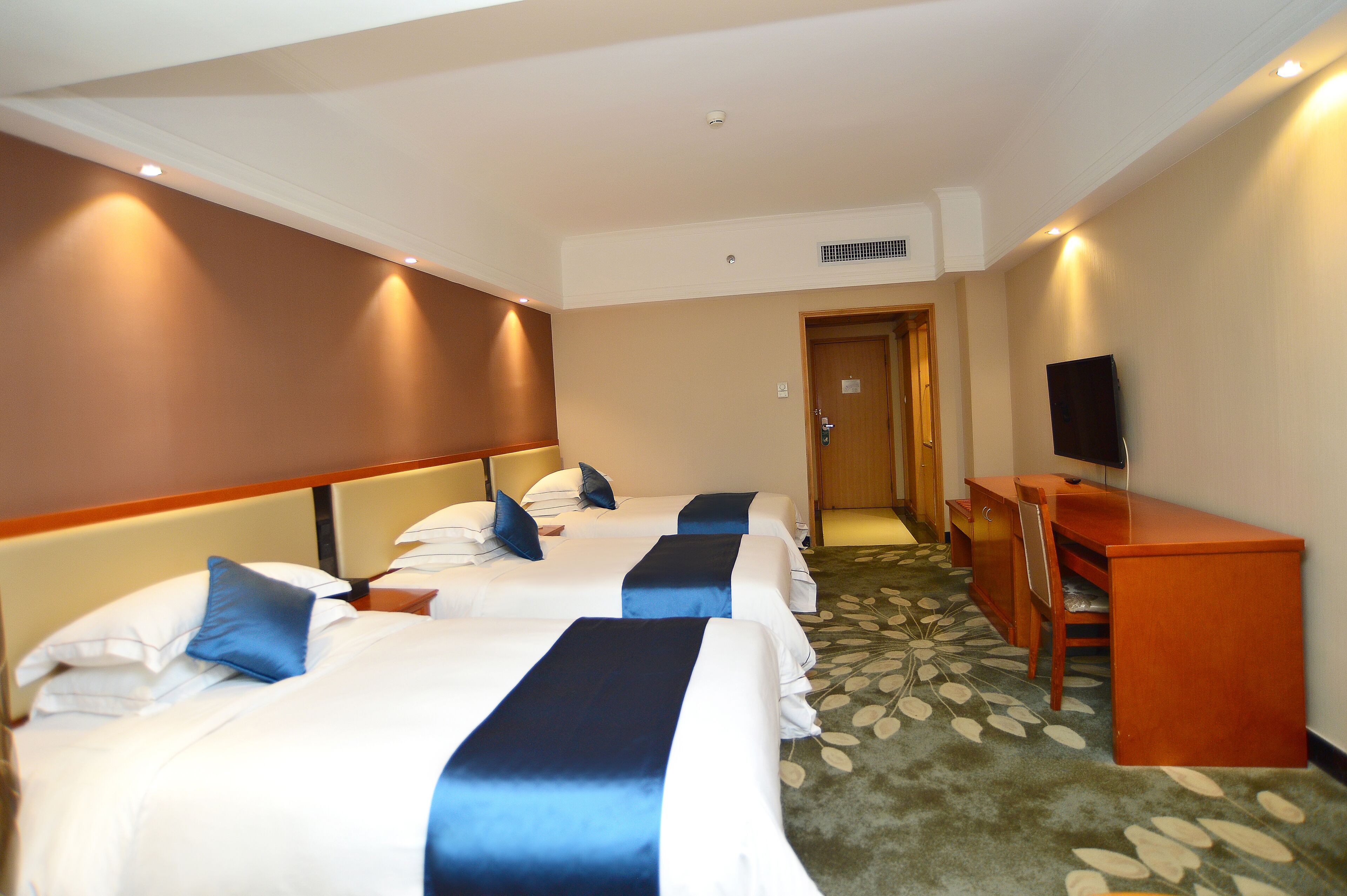 A hotel room with three beds, a desk, and a television.